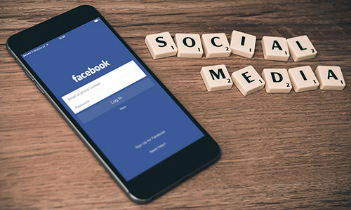 mobile phone open to facebook page with scrabble tiles on right spelling out Social Media